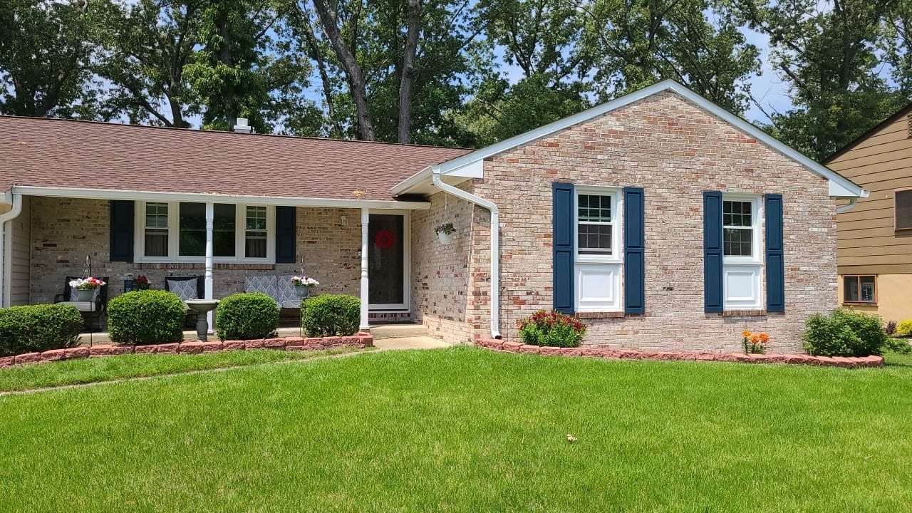 A brick house with blue shutters and green grass.