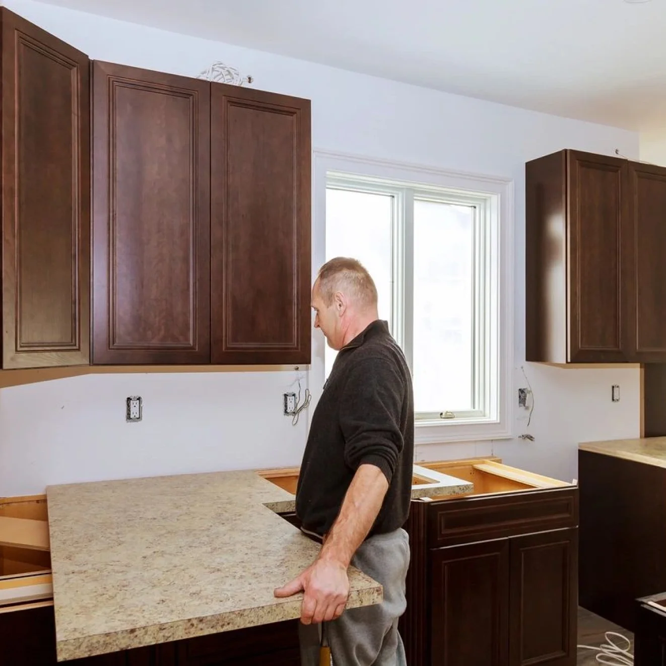 A man in black shirt and gray pants standing next to brown cabinets.