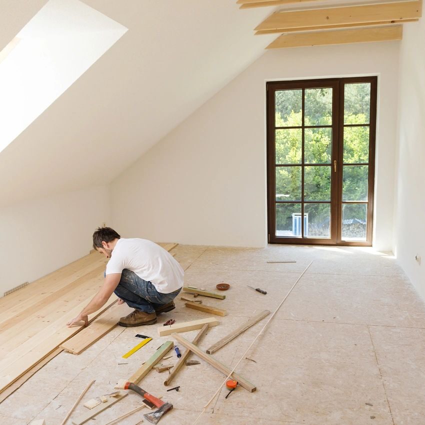 A man laying down wood in an unfinished room.